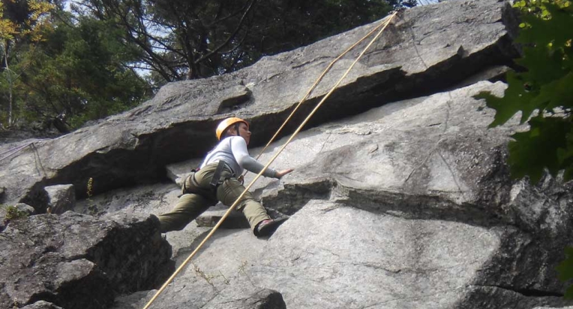 A person wearing safety gear is secured by ropes as they climb a rock wall. 